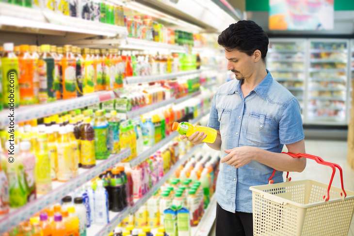 Mann steht vor Supermarktregal und studiert die Informationen auf einer Produktverpackung
